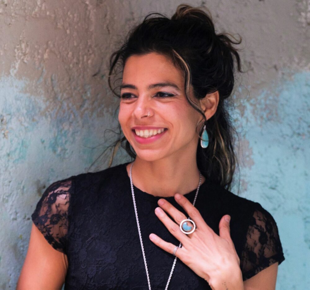 Smiling woman in a black shirt modelling Amazonite Halo Ring in sterling silver available wholesale from conscious woman owned artisan importer.